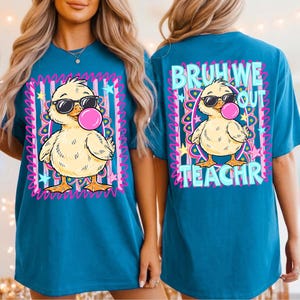 K&ouml;nnte beinhalten: T&uuml;rkisfarbenes T-Shirt mit einer Cartoon-Ente, die eine Sonnenbrille tr&auml;gt und eine Kaugummiblase bl&auml;st. Das Frontdesign ist mit rosa und lila Akzenten umrahmt. Auf der R&uuml;ckseite des Shirts steht der Text "BRUH WE OUT TEACHR".
