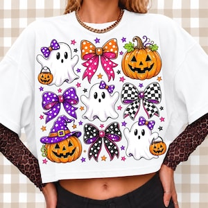 May include: A white short-sleeved t-shirt featuring a graphic print of three white ghosts, two orange jack-o'-lanterns, and four decorative bows in various patterns including polka dots and checkers, accented with small colourful stars.
