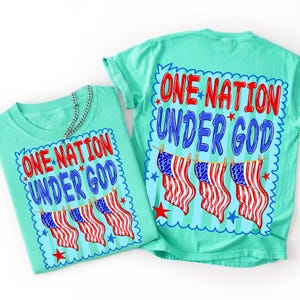 May include: A light mint green t-shirt featuring a graphic print with the text ONE NATION UNDER GOD in red and blue letters. Below the text, three American flags hang from a clothesline, surrounded by small red and blue stars on a striped background.