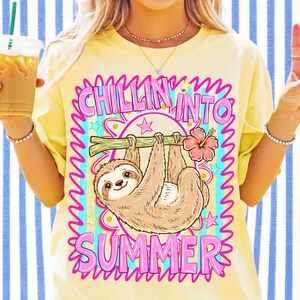 May include: A pale yellow t-shirt featuring a graphic of a brown sloth hanging from a green branch with a pink hibiscus flower. The text reads CHILLIN INTO SUMMER in bold pink letters, surrounded by small blue and pink stars on a striped background.