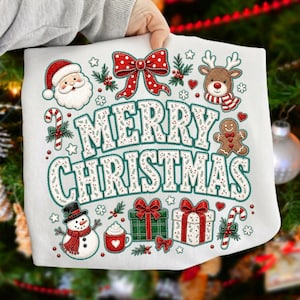 May include: A white sweatshirt featuring a colorful graphic with the text Merry Christmas in large letters. The design includes a Santa Claus, a reindeer, a gingerbread man, a snowman, gift boxes, candy canes, and a red bow with white dots.