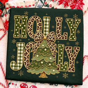 May include: A dark green sweatshirt featuring the embroidered text HOLLY JOLLY. The letters are filled with green polka dots, leopard print, and green gingham patterns. A central embroidered Christmas tree with a leopard print bow sits between the words.