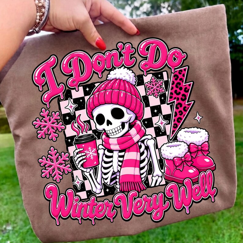 May include: A brown tote bag featuring a graphic of a skeleton wearing a pink beanie and scarf, holding a pink coffee cup. The design includes pink snowflakes, a leopard print lightning bolt, and the text I Don't Do Winter Very Well.