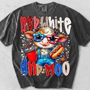 Puede incluir: Una camiseta gris carb&oacute;n con el gr&aacute;fico de una vaca que lleva gafas de sol en forma de estrella con un patr&oacute;n rojo, blanco y azul. La vaca sostiene una bebida roja y un perrito caliente, con el texto RED WHITE AND MOO en letras llamativas.