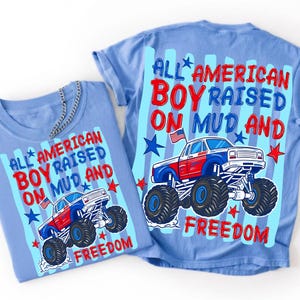 May include: A light blue t-shirt featuring a graphic of a red, white, and blue monster truck with a small American flag. The text reads ALL AMERICAN BOY RAISED ON MUD AND FREEDOM in red and blue lettering, accented by blue stars and stripes.