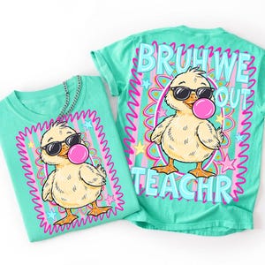 K&ouml;nnte beinhalten: Zwei t&uuml;rkisfarbene T-Shirts mit einer Cartoon-Ente, die eine Sonnenbrille tr&auml;gt und eine Blase bl&auml;st. Die Vorderseite des Shirts hat die Enten-Grafik in einem rosa und blauen Rahmen. Auf der R&uuml;ckseite des Shirts steht "BRUH WE OUT TEACHR".