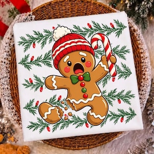 May include: A white t-shirt featuring a cartoon gingerbread person with a surprised expression, wearing a red and white knit hat and a green bow tie. The gingerbread person holds a red and white candy cane, surrounded by green pine branches.
