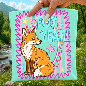 Op de afbeelding: Een licht mintgroene draagtas met een centrale illustratie van een oranje en witte vos. Het ontwerp bevat een roze geschulpte rand, lichtblauwe verticale strepen, gele en blauwe sterren en de tekst FOX YEAH! in lichtblauwe letters.