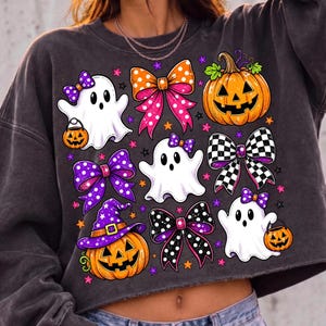 May include: A charcoal grey cropped sweatshirt featuring a graphic print of three white ghosts, two orange and yellow jack-o'-lanterns, and five decorative bows in various patterns including polka dots, checkered prints, and solid purple colours.