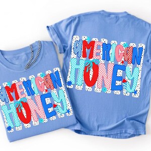 May include: Two light blue t-shirts featuring a graphic print with the text AMERICAN HONEY in red, white, and blue patterns including polka dots and checkers. The design includes small blue flowers and firework icons on a white striped background.