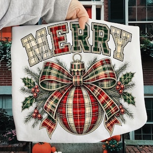 Puede incluir: Una superficie de tela blanca con un estampado gr&aacute;fico de un adorno navide&ntilde;o con un gran lazo a cuadros. La palabra MERRY est&aacute; impresa en una fuente de estilo universitario con patr&oacute;n de cuadros sobre el adorno, rodeada de acebo y bayas rojas.