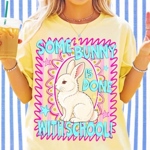 K&ouml;nnte beinhalten: Ein blassgelbes T-Shirt mit einer Grafik eines wei&szlig;en Kaninchens in einem rosa ovalen Rahmen. Der Text SOME BUNNY IS DONE WITH SCHOOL! steht in hellblauen Buchstaben, umgeben von rosa geschl&auml;ngelten R&auml;ndern und kleinen blauen und gelben Sternen.