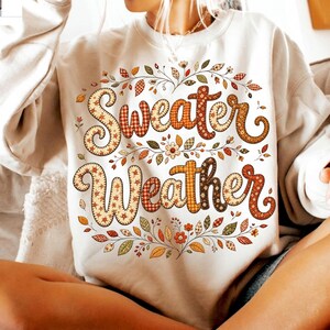 Pu&ograve; includere: Una felpa girocollo color crema con la scritta Sweater Weather in un carattere decorativo a motivi vari. Il testo &egrave; circondato da una disposizione circolare di foglie autunnali colorate, piccoli fiori e sottili rami intrecciati.