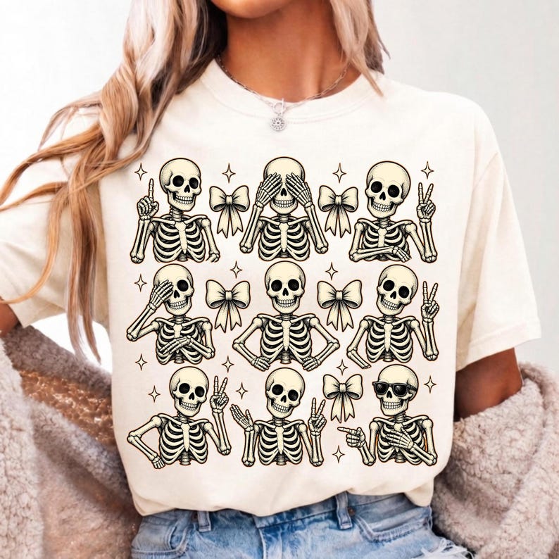 May include: A cream-colored t-shirt featuring a repeating graphic print of nine skeletons in various poses. The skeletons are depicted with different hand gestures, some wearing sunglasses, and are interspersed with small star shapes and cream-colored bows.
