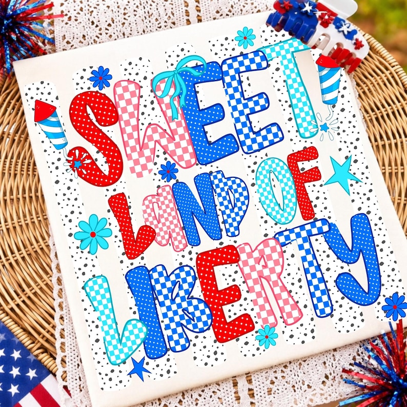 K&ouml;nnte beinhalten: Ein wei&szlig;es T-Shirt mit dem Text SWEET LAND OF LIBERTY in einer Mischung aus roten, wei&szlig;en und blauen Mustern, einschlie&szlig;lich Punkten und Karos. Das Design enth&auml;lt kleine blaue Blumen, hellblaue Sterne und rote und blaue Feuerwerksmotive.