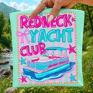 Może przedstawiać: Jasnozielony kwadrat z tkaniny w kolorze miętowym z r&oacute;żowo-miętowymi paskami w tle oraz napisem REDNECK YACHT CLUB pogrubionymi r&oacute;żowymi i niebieskimi literami. Zawiera r&oacute;żową kokardę, niebieskie i r&oacute;żowe gwiazdki oraz grafikę łodzi pontonowej.