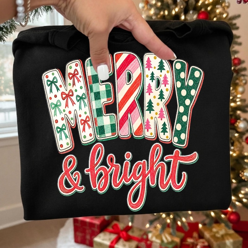 May include: A black sweatshirt featuring the text Merry & bright. The word Merry is in large block letters with varied patterns: red bows, green plaid, red and white candy cane stripes, pink and green trees, and green polka dots. Bright is in red.