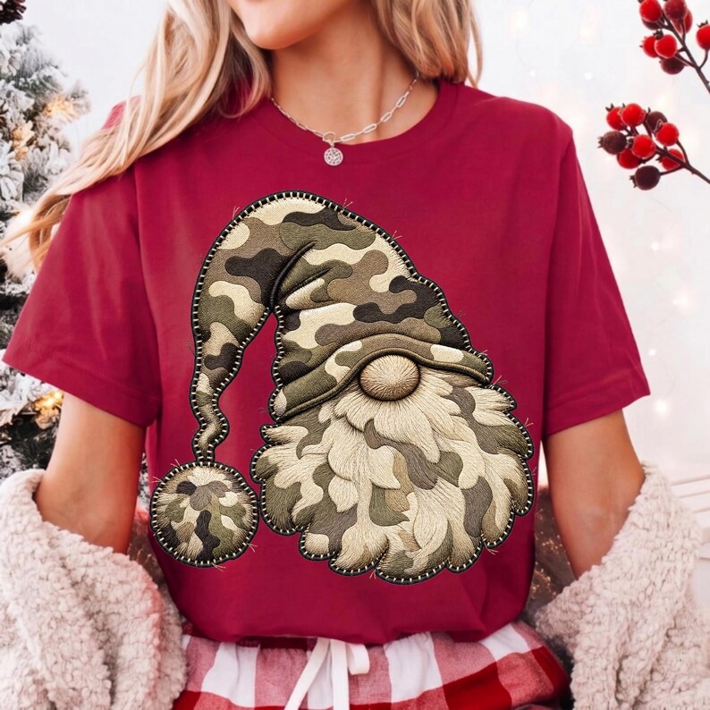 K&ouml;nnte beinhalten: Ein kastanienbraunes Kurzarm-T-Shirt mit einer gro&szlig;en Stickerei eines Gnoms, der eine M&uuml;tze mit Camouflage-Muster tr&auml;gt. Der Gnom hat einen strukturierten, hellen Bart und einen passenden Camouflage-Bommel am Ende der langen, herabh&auml;ngenden M&uuml;tze.