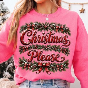 May include: A bright pink crewneck sweatshirt featuring a graphic print of green pine branches, red berries, and red bows arranged in horizontal bands. The text "Christmas Please" is printed in a bold, red, stylized font across the center.