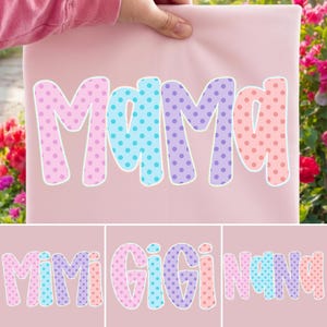 Puede incluir: Una tela rosa claro con la palabra "Mama" en letras grandes y coloridas con lunares. Las letras est&aacute;n delineadas en blanco. Debajo, tres im&aacute;genes adicionales con las palabras "Mimi Gigi Nana" en el mismo estilo.