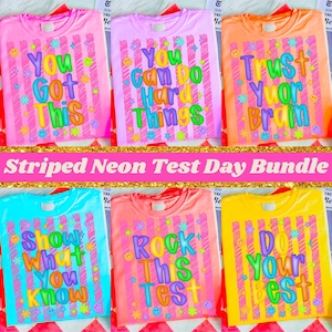 May include: A collection of six neon-colored t-shirts with positive messages. Each shirt features a different phrase in colorful bubble letters, such as "You Got This" and "Do Your Best", with decorative stars and smiley faces. The shirts have vertical stripes.