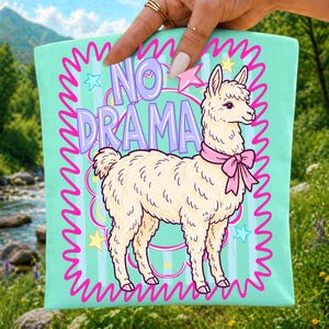 Peut inclure: Un sac fourre-tout vert menthe clair orn&eacute; d'une illustration de lama cr&egrave;me avec un n&oelig;ud rose autour du cou. Le motif comprend le texte violet NO DRAMA, entour&eacute; d'une bordure rose vif ondul&eacute;e, d'&eacute;toiles jaunes et bleues, et de rayures.