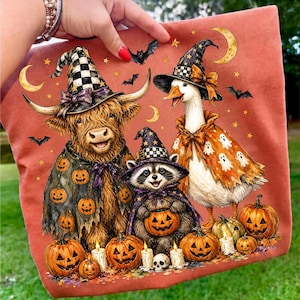 May include: A burnt orange fabric featuring a graphic print of a Highland cow, a raccoon, and a goose wearing witch hats and capes. The scene includes pumpkins, bats, stars, and crescent moons. The animals are decorated with Halloween motifs.