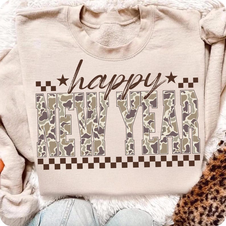 May include: A beige sweatshirt with the words "happy NEW YEAR" in a brown font. The words "NEW YEAR" are filled with a camouflage pattern. The word "happy" has a star on each side. A brown checkered pattern is at the top and bottom of the words.