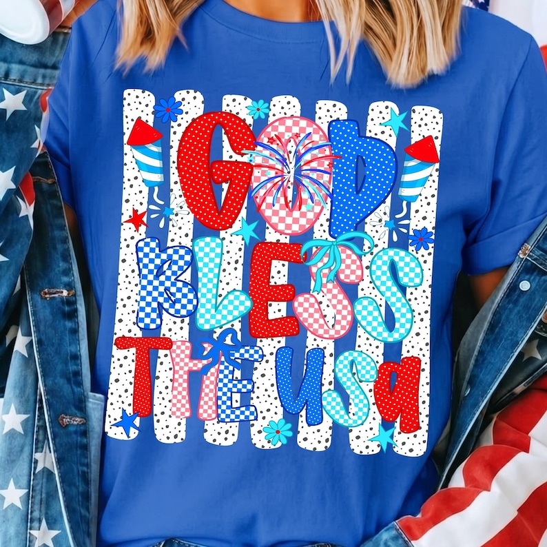 K&ouml;nnte beinhalten: Ein k&ouml;nigsblaues T-Shirt mit einem Grafikdruck und dem Text GOD BLESS THE USA. Das Design enth&auml;lt rote, wei&szlig;e und blaue Muster, Punkte, Karomuster, Feuerwerksdarstellungen sowie kleine Stern- und Blumenformen auf der gesamten Fl&auml;che.