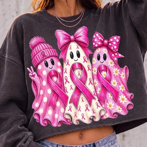 Puede incluir: Una sudadera gris carb&oacute;n de manga larga con un gr&aacute;fico de tres fantasmas. El fantasma de la izquierda lleva un gorro rosa con pomp&oacute;n, el central tiene un lazo rosa grande y el de la derecha un lazo rosa de lunares. Cada fantasma muestra un lazo rosa.