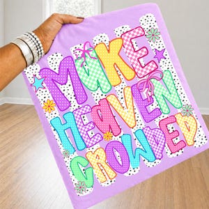 May include: A light purple fabric square featuring the text MAKE HEAVEN CROWDED in colorful, patterned block letters. The design includes polka dots, checkerboard patterns, pink bows, small stars, and flowers against a black and white spotted background.