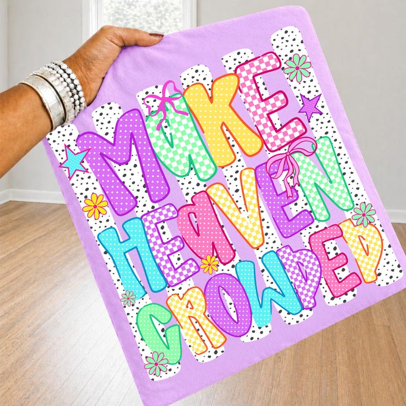 May include: A light purple fabric square featuring the text MAKE HEAVEN CROWDED in colorful, patterned block letters. The design includes polka dots, checkerboard patterns, pink bows, small stars, and flowers against a black and white spotted background.