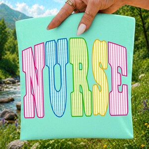 以下が含まれることがあります： 明るいミントグリーンの布製アイテムで、大きく太いアーチ状の文字で「NURSE」とプリントされています。各文字はピンク、青、ライムグリーン、黄色などの異なる色で、細い垂直の白いストライプ模様が施されています。