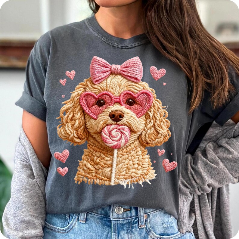 May include: Dark grey t-shirt featuring a cartoon poodle with heart-shaped sunglasses, a pink bow, and a lollipop. Pink hearts surround the poodle. The design is a whimsical and cute graphic.