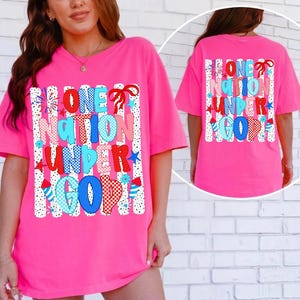 Pu&ograve; includere: Una t-shirt a maniche corte rosa acceso con una stampa grafica che riporta il testo ONE NATION UNDER GOD in lettere con motivi rossi, blu e bianchi. Il design include strisce verticali, motivi a fuochi d'artificio e piccoli fiocchi rossi.