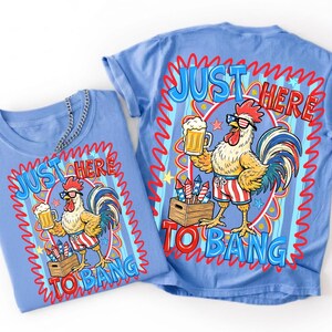 Op de afbeelding: Een lichtblauw t-shirt met een afbeelding van een haan met een zonnebril en een korte broek in Amerikaanse vlagstijl, die een bierpul vasthoudt naast een kist met vuurwerk. De tekst "JUST HERE TO BANG" staat in blauw en rood op het shirt.