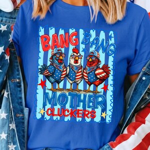 May include: A royal blue t-shirt featuring a graphic of three chickens wearing star-spangled bandanas and sunglasses. The text reads BANG BANG MOTHER CLUCKERS. The design includes red, white, and blue stripes, stars, and patriotic color schemes.