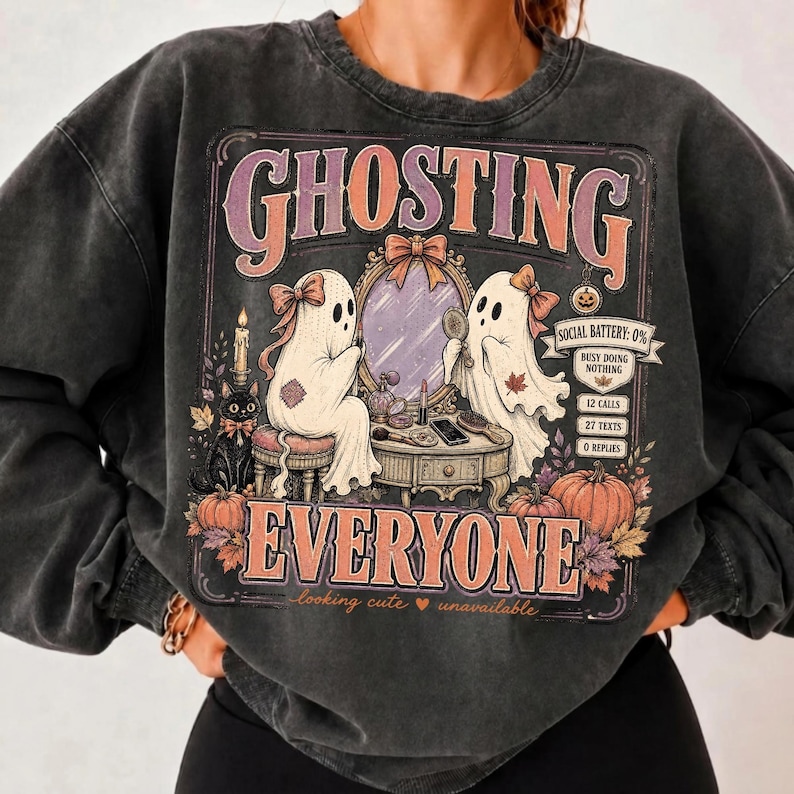 May include: A charcoal gray crewneck sweatshirt featuring a graphic print of two ghosts at a vanity mirror. The text reads GHOSTING EVERYONE, SOCIAL BATTERY: 0%, BUSY DOING NOTHING, 12 CALLS, 27 TEXTS, 0 REPLIES, and looking cute unavailable.