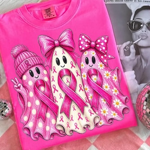 Puede incluir: Una camiseta de color rosa brillante con un gr&aacute;fico de tres fantasmas. El primer fantasma lleva un gorro rosa con un lazo, el segundo tiene un lazo rosa grande y el tercero un lazo de lunares con margaritas. Cada fantasma muestra un lazo rosa.