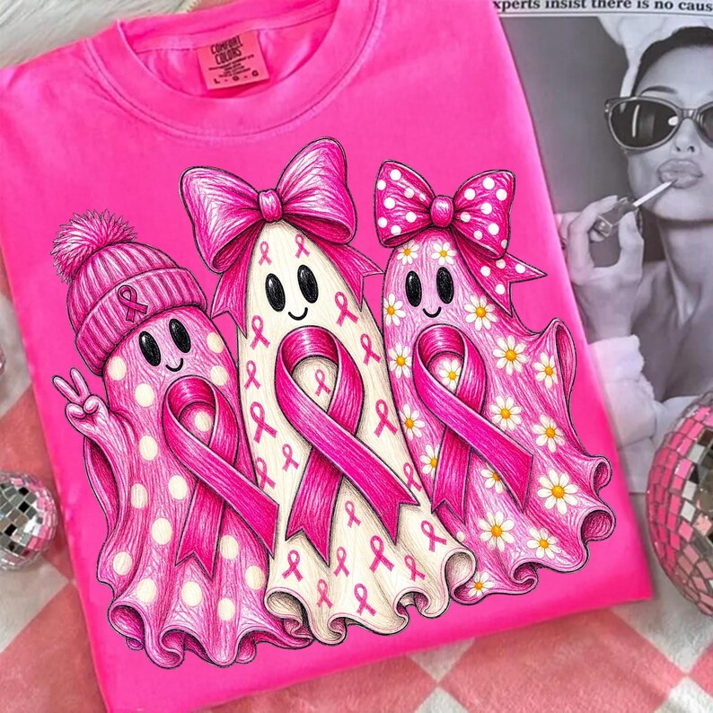Puede incluir: Una camiseta de color rosa brillante con un gr&aacute;fico de tres fantasmas. El primer fantasma lleva un gorro rosa con un lazo, el segundo tiene un lazo rosa grande y el tercero un lazo de lunares con margaritas. Cada fantasma muestra un lazo rosa.