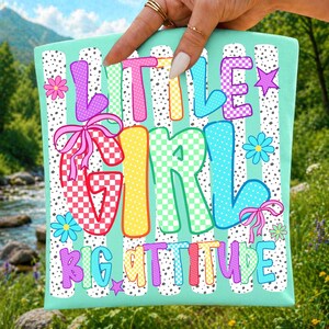 May include: A light teal fabric panel featuring the text LITTLE GIRL BIG ATTITUDE in colorful, patterned block letters. The design includes white vertical stripes with black dots, pink bows, and small flowers and stars in various bright colors.