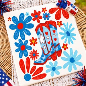 K&ouml;nnte beinhalten: Ein quadratischer Stoffaufn&auml;her in Wei&szlig; mit einem Grafikdruck von zwei Cowboystiefeln in Rot, Wei&szlig; und Blau mit Herz- und Sternmustern, umgeben von verschiedenen stilisierten roten und blauen Blumen auf einem wei&szlig;en, patriotisch gestalteten Hintergrund.