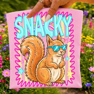 May include: A light pink fabric pouch featuring a graphic of a brown squirrel wearing bright blue sunglasses. The word SNACKY is printed in large light blue letters above the squirrel. The design includes a pink squiggly border and stars.
