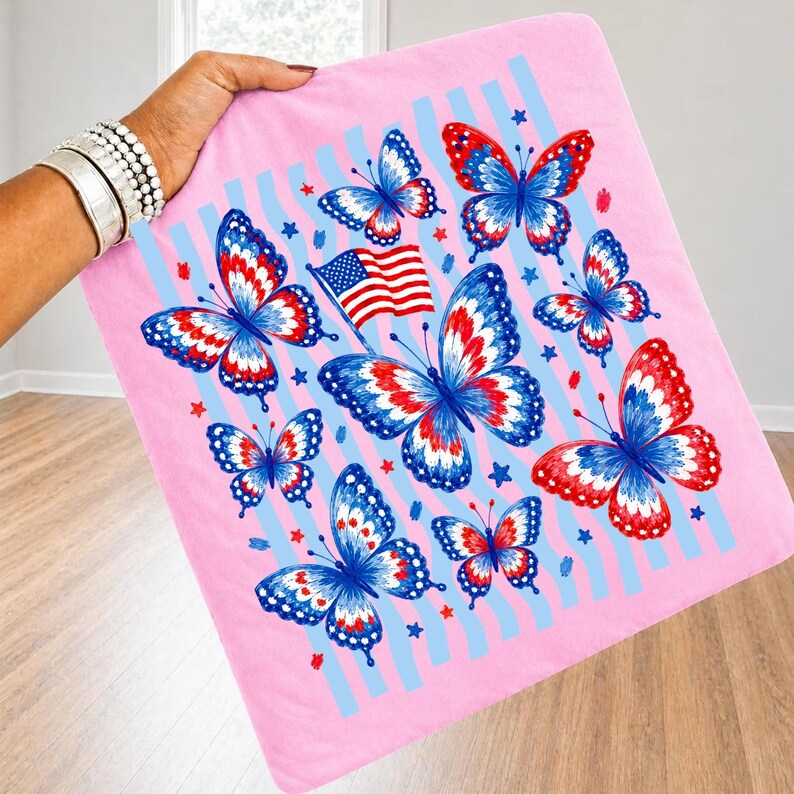 Puede incluir: Un art&iacute;culo de tela rosa de forma cuadrada con un patr&oacute;n de mariposas de alas rojas, blancas y azules. El dise&ntilde;o incluye una peque&ntilde;a bandera estadounidense y estrellas rojas y azules dispersas sobre rayas verticales azul claro en el fondo.