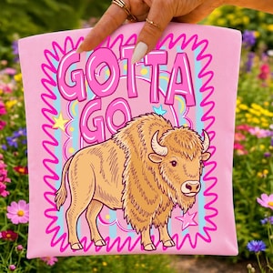 May include: A light pink fabric item featuring a graphic illustration of a brown bison. The text "GOTTA GO" is printed in large, bold pink letters above the bison. The design includes a bright pink squiggly border and small yellow and pink stars.