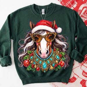 May include: A dark green crewneck sweatshirt featuring a graphic of a horse wearing a red Santa hat, leopard print sunglasses, and a decorative necklace made of turquoise stones, gold bells, red ornaments, and green holly leaves.