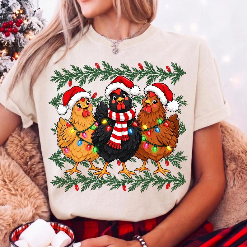 Puede incluir: Una camiseta de color crema con un gr&aacute;fico de tres pollos que llevan gorros de Pap&aacute; Noel rojos y blancos. Los pollos est&aacute;n envueltos en luces de Navidad de colores y el pollo central lleva una bufanda a rayas rojas y blancas.