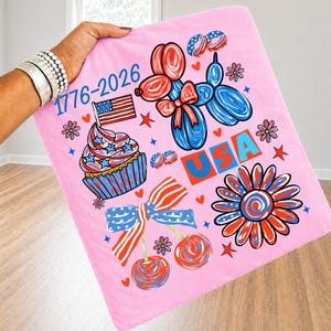 May include: A light pink fabric square featuring a patriotic graphic print with the text 1776-2026 and USA. The design includes a red and blue balloon dog, a cupcake with an American flag, a striped bow, cherries, and a large flower in red and blue.