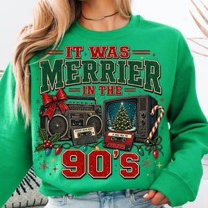 Może przedstawiać: Jaskrawozielona bluza z grafiką i napisem IT WAS MERRIER IN THE 90'S. Wz&oacute;r przedstawia zabytkowy radiomagnetofon z czerwoną kokardą, telewizor retro z choinką, kasety magnetofonowe oraz sznur lampek choinkowych.