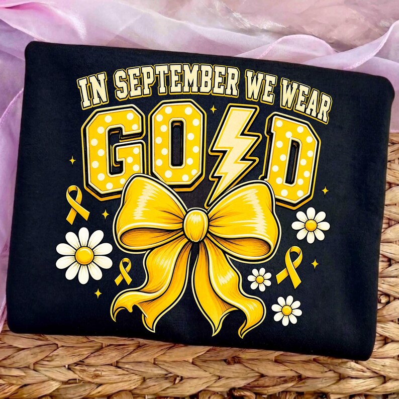 May include: A black t-shirt featuring the text IN SEPTEMBER WE WEAR GOLD in yellow with white polka dots. The design includes a large yellow bow, a lightning bolt replacing the letter L, small yellow awareness ribbons, and white daisy flowers.
